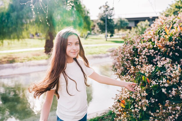 Pretty girl touching flowers near lake in park