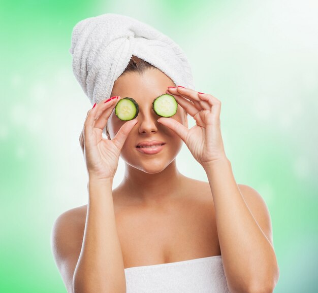 Pretty girl in towel holding cut cucumber on eyes.