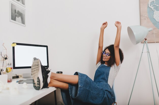 Pretty girl in vintage denim clothes relaxing with legs on table and hands up