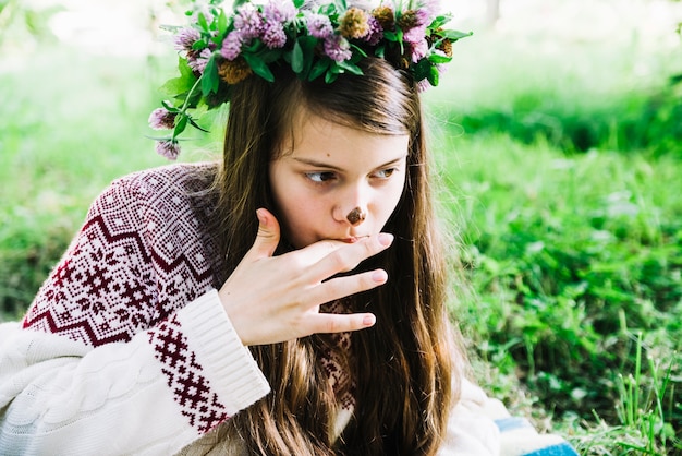 Pretty girl wearing wreathe on head licking her fingers with chocolate stain on nose