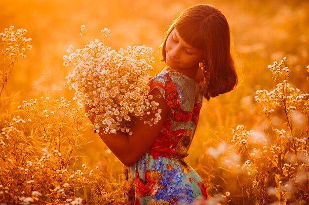 Pretty girl with a bouquet stands on the evening field 