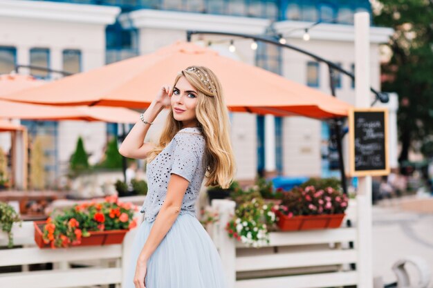 Pretty girl with long blonde hair smiling to camera on terrace background.