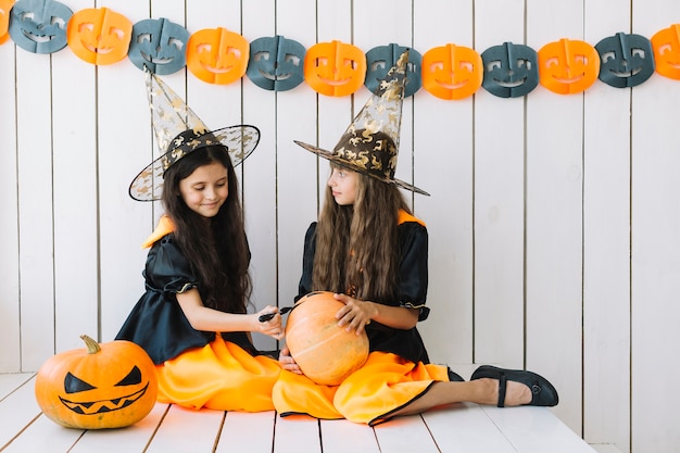 Pretty Halloween witches decorating pumpkin