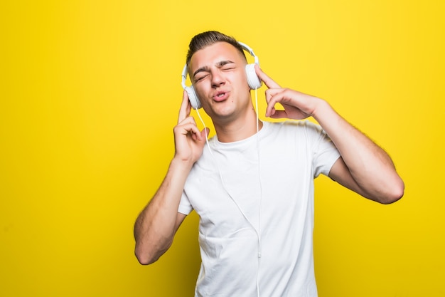 Pretty handsome young man in white t-shirt listen music with his new earphones isolated on yellow wall