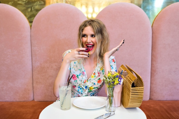 Pretty happy blonde hipster woman eating  tasty raspberry dessert cake, sitting at cute bakery, enjoy her meal, sweet breakfast, diet nutrition concept.