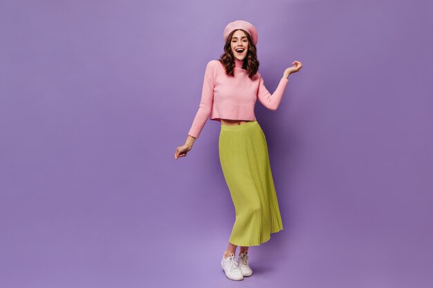 Довольно счастливая кудрявая женщина танцует на фиолетовой стене
