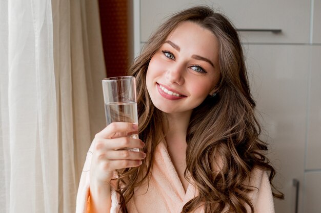 自宅で新鮮な水を飲むバスローブでかなり幸せな女