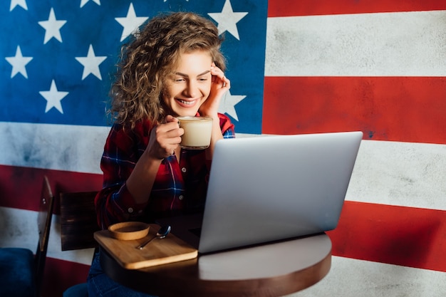 Foto gratuita donna graziosa e felice che usa il computer portatile mentre è seduto al bar. giovane donna seduta in una caffetteria e lavorando sul computer portatile.