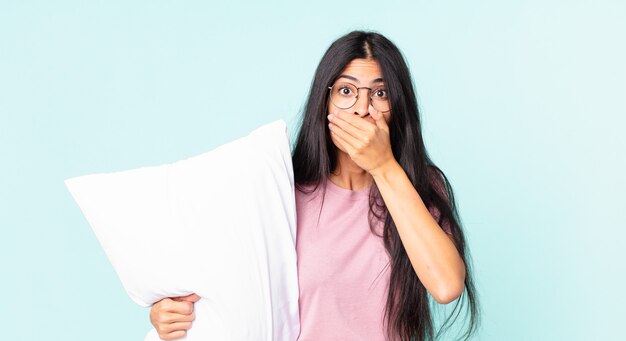 ショックを受けて枕でパジャマを着て手で口を覆うかなりヒスパニック系の女性
