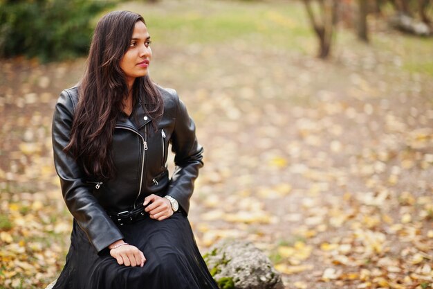 Красивая индийская девушка в черном платье сари и кожаной куртке позирует на осенней улице