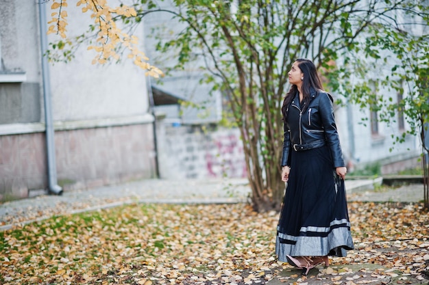 秋の通りで屋外でポーズをとった黒いサリードレスと革のジャケットのかわいいインドの女の子