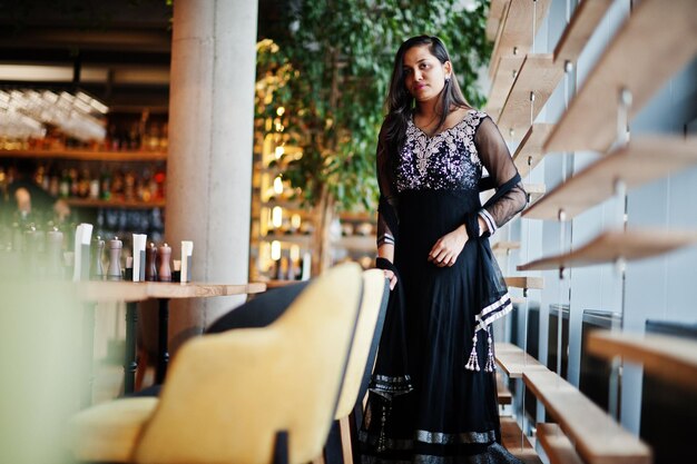 Симпатичная индийская девушка в черном платье сари позирует в ресторане