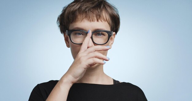 Pretty joyful smiling young woman with dark short hair wearing a black top and glasses isolated on color backgrounds