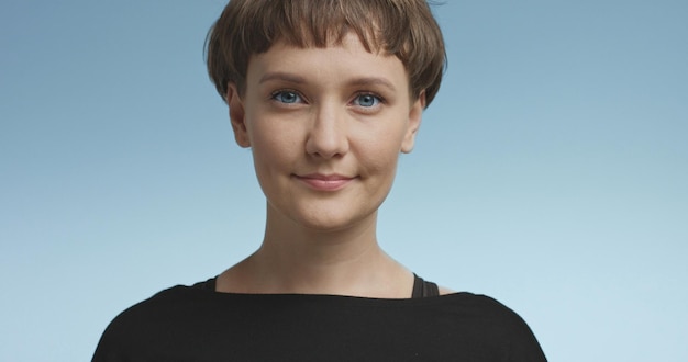 Pretty joyful smiling young woman with dark short hair wearing a black top and glasses isolated on color backgrounds