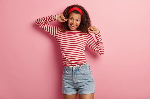Довольно радостная девочка-подросток с вьющимися волосами позирует в полосатом красном свитере
