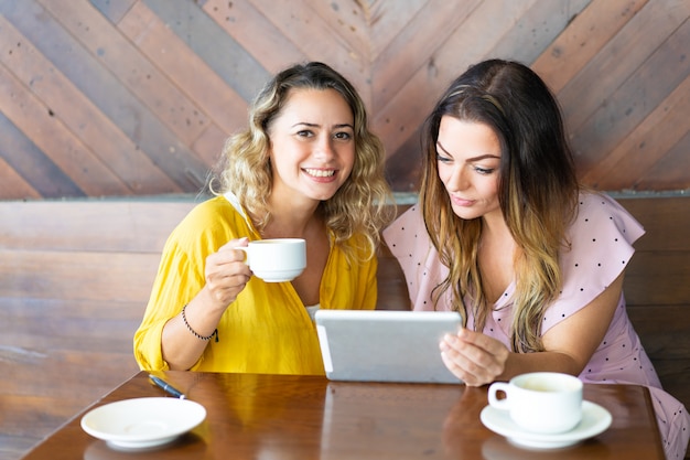 Pretty ladies using tablet computer and drinking coffee in cafe