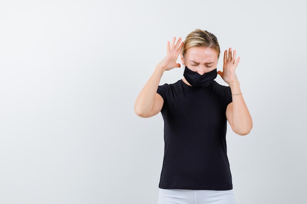 Pretty lady in black t-shirt, black mask keeping raised hands isolated