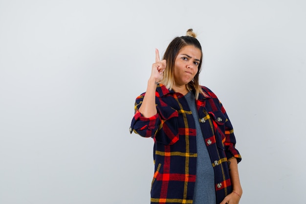 Pretty lady in casual shirt pointing up and looking serious , front view.