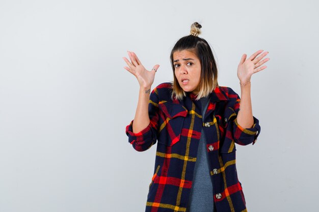 Pretty lady in casual shirt showing palms in surrender gesture and looking terrified , front view.