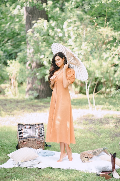 傘を保持し、昼間は自然の中でオレンジ色のドレスを探しているきれいな女性。