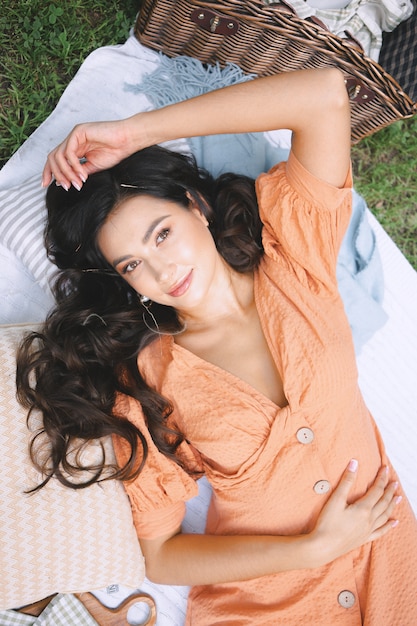 Pretty lady in orange dress lying and looking in nature during daytime .