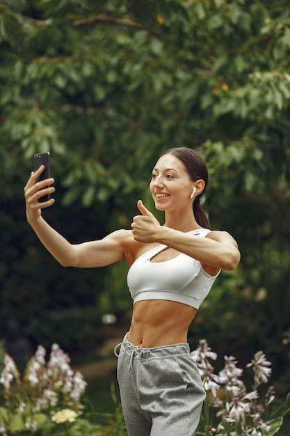 Pretty lady in a park. Brunette with mobile phone. Girl in a sportsuit.