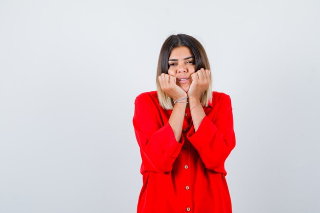 Pretty lady pillowing face on her hands in red blouse and looking curious. front view.