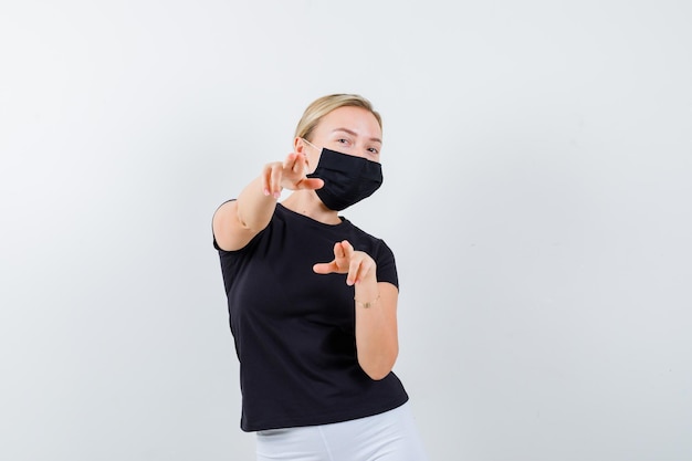 Pretty lady pointing at camera in black t-shirt, black mask isolated