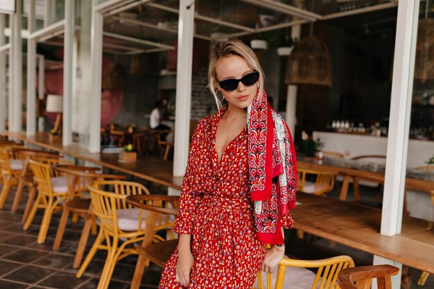 Красивая дама позирует в летнем кафе в ярком летнем платье, солнцезащитных очках и аксессуарах