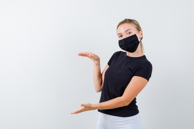 Pretty lady showing large size sign in black t-shirt, black mask isolated