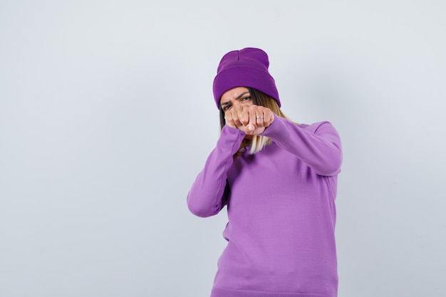 Pretty lady standing in fight pose in sweater, beanie and looking confident. front view.
