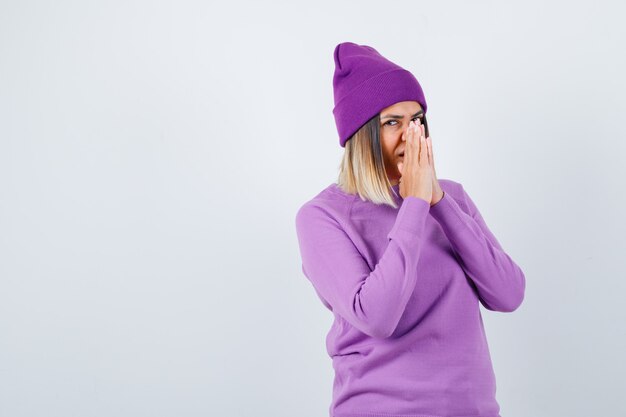 Pretty lady in sweater, beanie with hands in praying gesture and looking dreamy , front view.