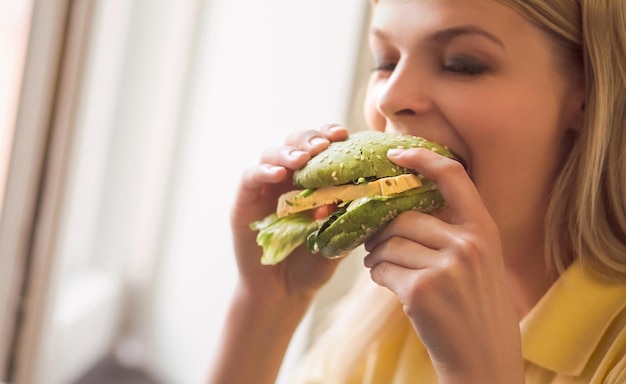 Pretty lady on vegan diet Healthy food concept Closeup image of blond woman eating vegan burger in vegan restaurant or cafe