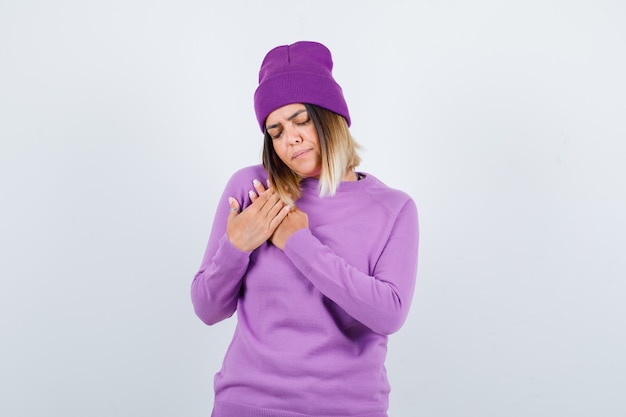 Free photo pretty lady with hands on chest in sweater, beanie and looking upset , front view.