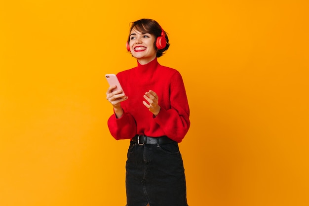 Pretty laughing woman holding smartphone on yellow wall