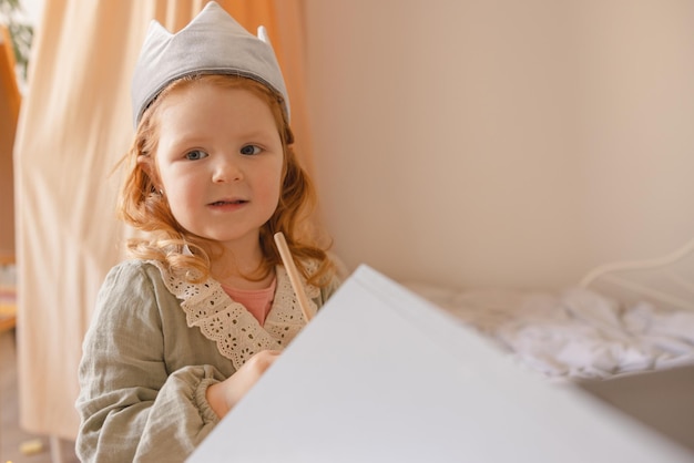 Pretty little caucasian girl with red hair wears casual clothes indoors Children lifestyle concept