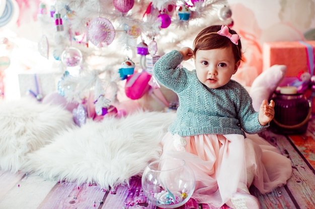 Pretty little child sits on fluffy carpet before Christmas tree 