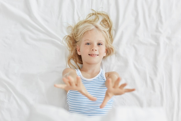침대에 누워있는 동안 그녀의 손을 스트레칭 예쁜 아이. 침대에서 휴식을 갖는 푸른 눈의 작은 소녀