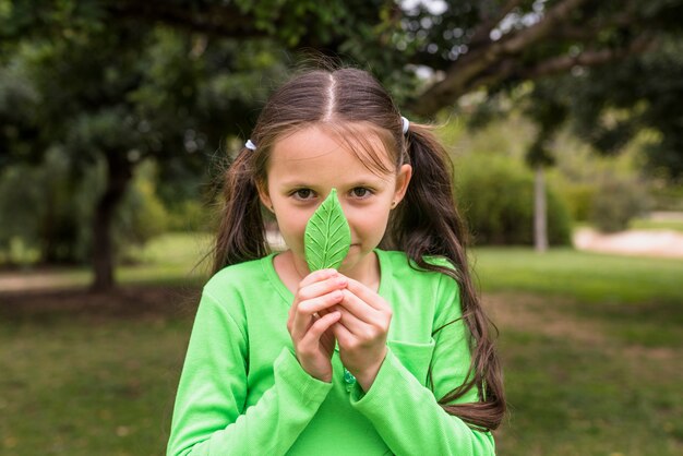 Pretty little girl holding artificial green leaf in front of her nose