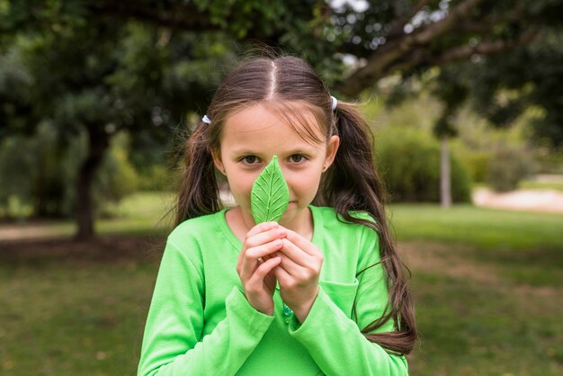 Хорошенькая девочка держит искусственный зеленый лист перед ее носом