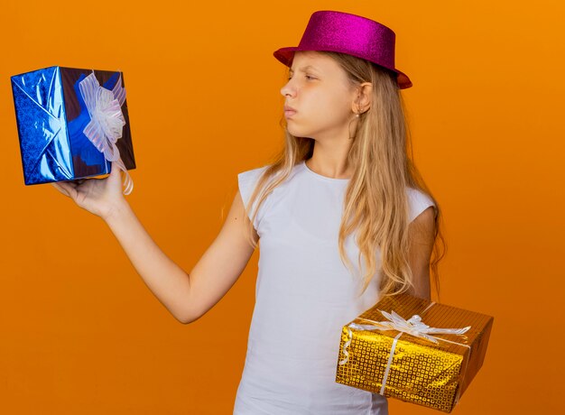 Pretty little girl in holiday hat holding gift boxes