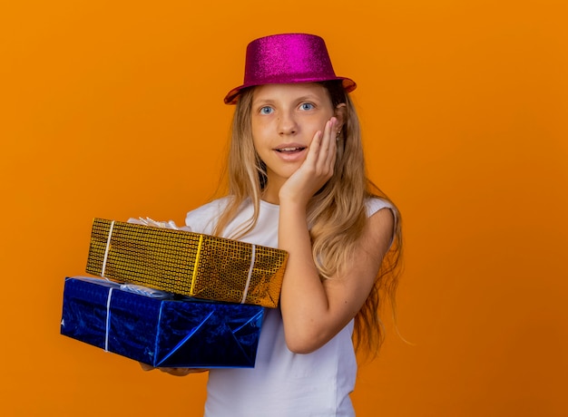 Pretty little girl in holiday hat holding gift boxes