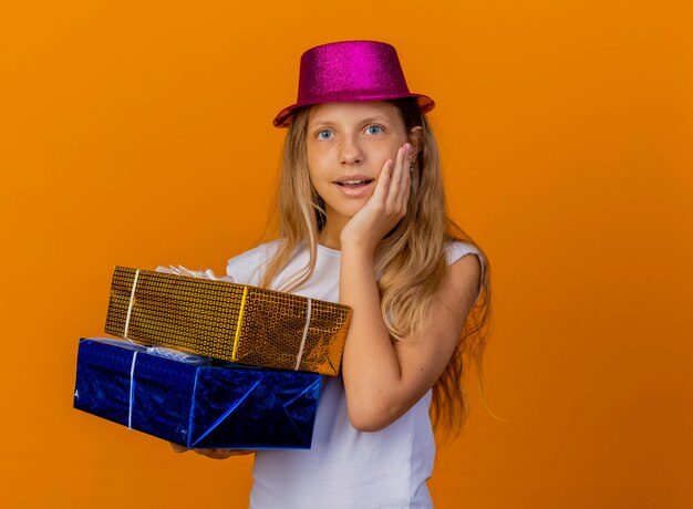 Pretty little girl in holiday hat holding gift boxes