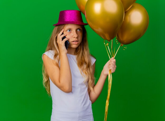 Симпатичная маленькая девочка в праздничной шляпе, держащей смартфон