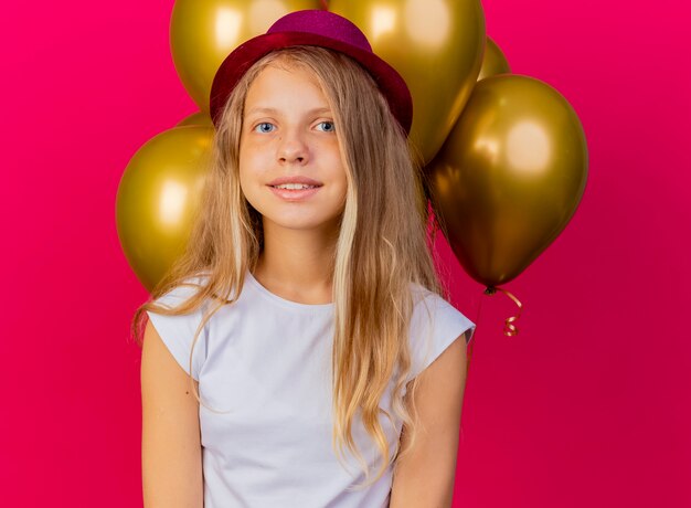 쾌활하게 웃고있는 baloons의 무리와 함께 휴가 모자에 예쁜 소녀