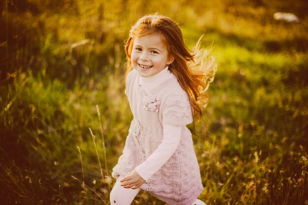 Pretty little girl with red hair plays with fallen leaves 