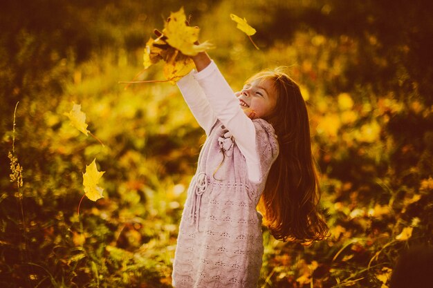 Pretty little girl with red hair plays with fallen leaves 