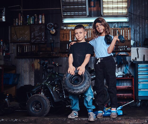 Pretty little kids are holding weel and screwdriver while posing for photographer at auto service.