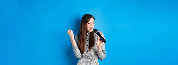 Free photo pretty natural girl in dress singing songs in microphone holding mic and looking passionate while pe