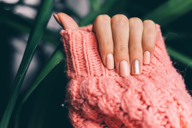 Pretty nude color manicure, one finger shiny golden, on knitted pink wool pillover background